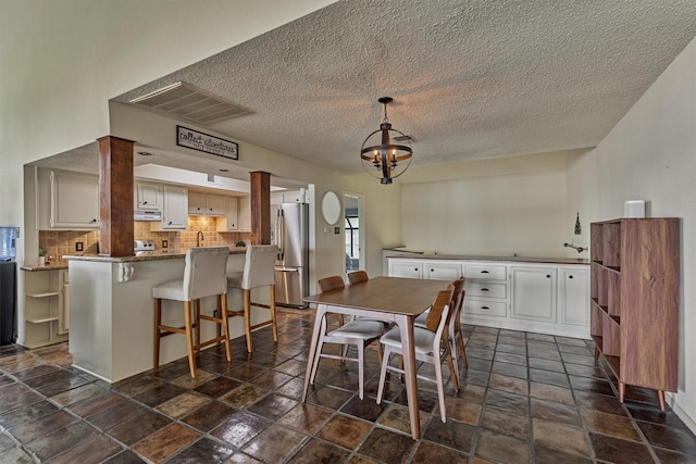 dining area featuring a chandelier, a textured ceiling, visible vents, and stone tile flooring