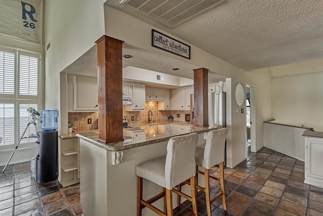 kitchen with light stone counters, a kitchen breakfast bar, a textured ceiling, stone tile floors, and tasteful backsplash