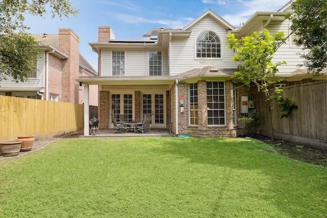 rear view of house featuring brick siding, a patio, a fenced backyard, solar panels, and a lawn