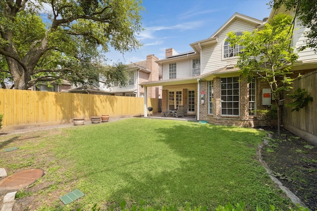 back of property featuring a yard, a chimney, brick siding, a patio area, and a fenced backyard