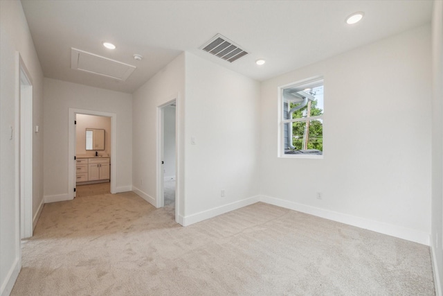 unfurnished bedroom with light carpet, ensuite bath, attic access, baseboards, and visible vents