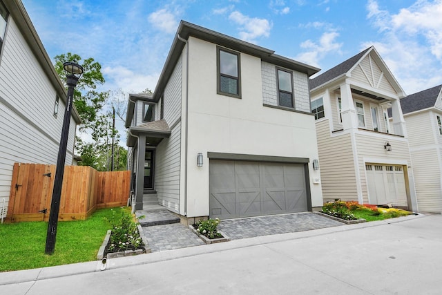 view of front facade with fence, an attached garage, driveway, and stucco siding