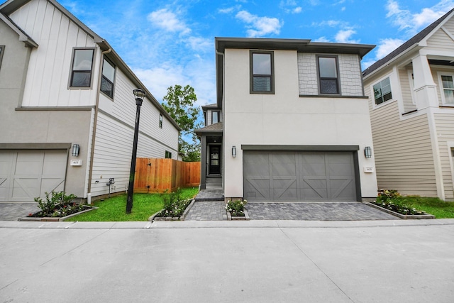 view of front of house with fence, an attached garage, board and batten siding, stucco siding, and decorative driveway