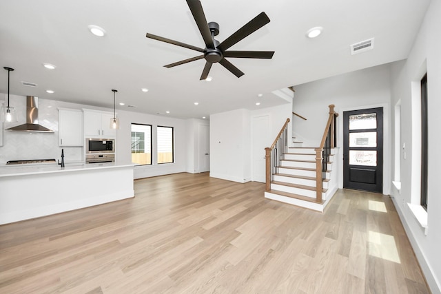 unfurnished living room with visible vents, stairs, recessed lighting, a ceiling fan, and light wood-style flooring