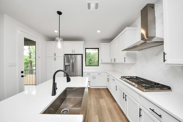 kitchen featuring visible vents, wall chimney range hood, light wood-type flooring, a sink, and stainless steel appliances