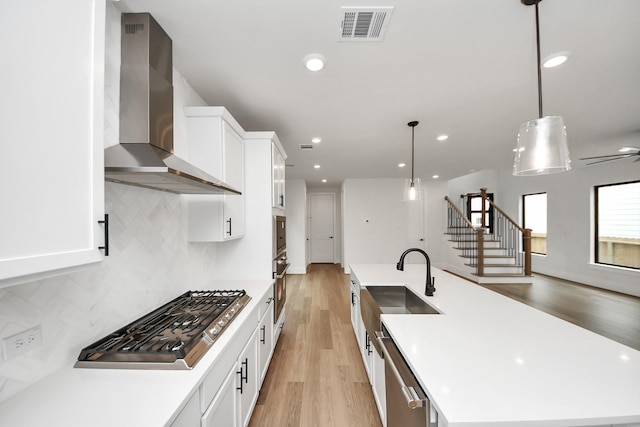 kitchen featuring visible vents, a kitchen island with sink, wall chimney exhaust hood, a sink, and stainless steel appliances