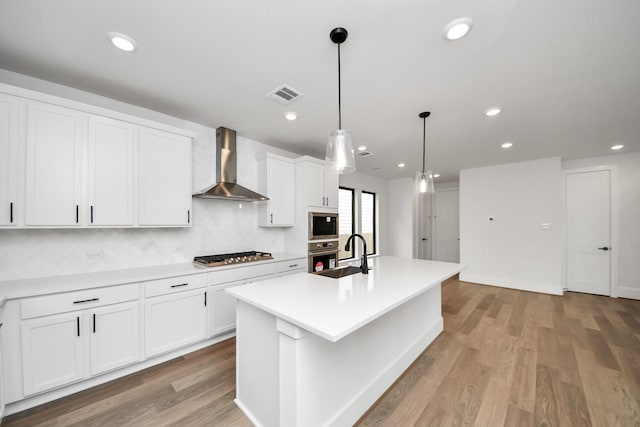 kitchen with wall chimney range hood, stainless steel appliances, white cabinetry, light wood-type flooring, and visible vents