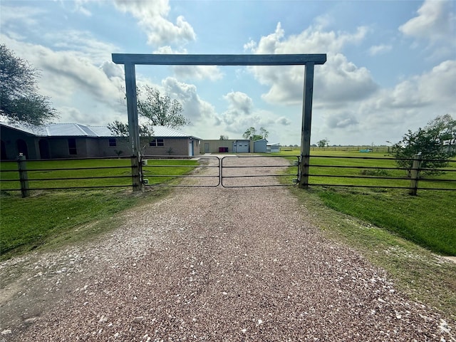 view of gate with fence, a yard, and a rural view