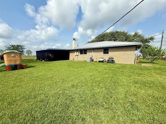 back of property with cooling unit, a chimney, brick siding, metal roof, and a lawn