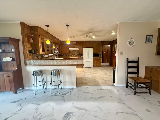 kitchen with a sink, freestanding refrigerator, a peninsula, a ceiling fan, and glass insert cabinets