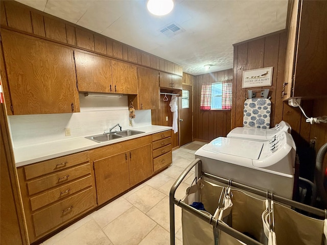 kitchen featuring brown cabinetry, visible vents, wooden walls, separate washer and dryer, and a sink