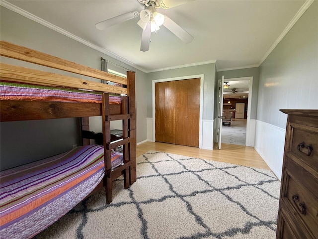 bedroom with crown molding, a closet, wood finished floors, ceiling fan, and a wainscoted wall