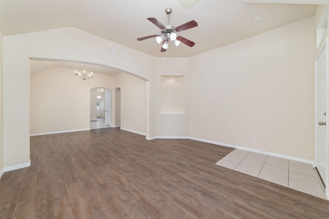 unfurnished room with arched walkways, ceiling fan with notable chandelier, baseboards, wood finished floors, and vaulted ceiling