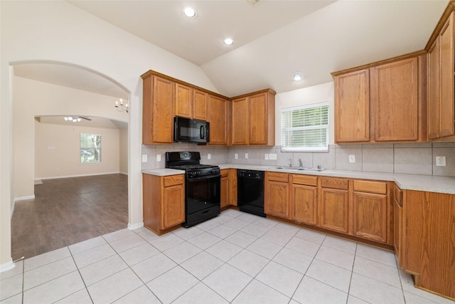 kitchen with decorative backsplash, light countertops, a sink, black appliances, and vaulted ceiling