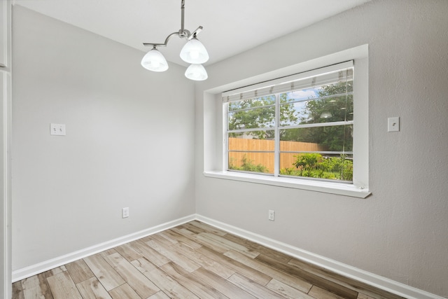 spare room with baseboards, wood finished floors, and a notable chandelier