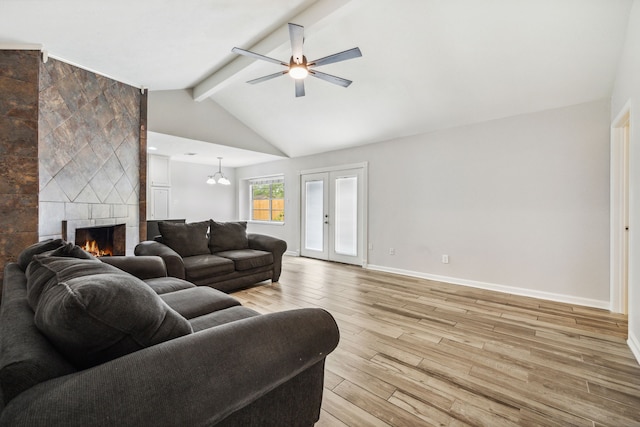 living room featuring baseboards, lofted ceiling with beams, light wood-type flooring, a tile fireplace, and a ceiling fan