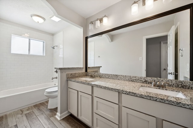 bathroom featuring a sink, washtub / shower combination, wood finished floors, and toilet