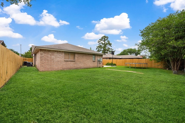 view of yard with a fenced backyard, a trampoline, and central air condition unit