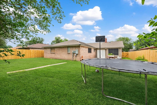 rear view of house featuring a fenced backyard, a trampoline, a yard, and brick siding