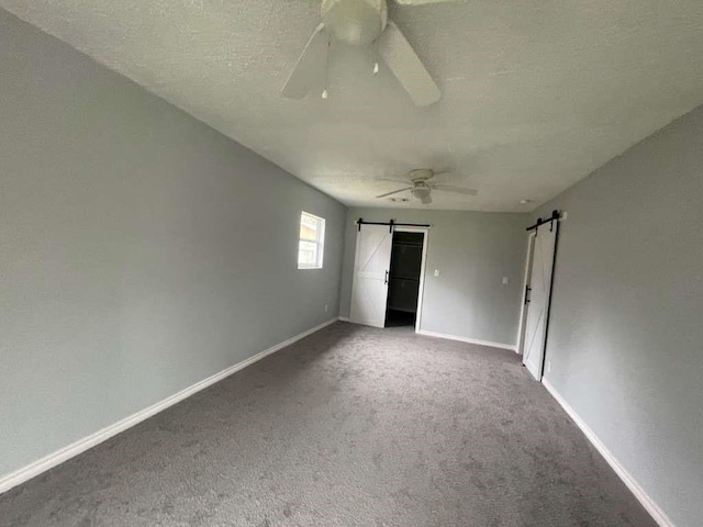 unfurnished bedroom featuring a ceiling fan, a textured ceiling, a barn door, carpet floors, and baseboards