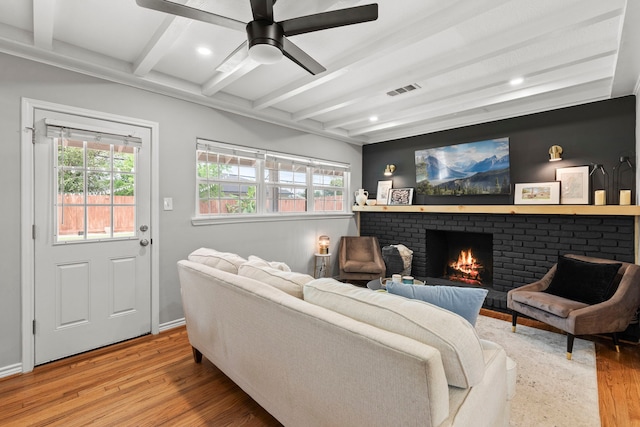 living area with light wood finished floors, a brick fireplace, a wealth of natural light, and beamed ceiling