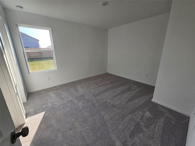 unfurnished room featuring dark colored carpet and baseboards
