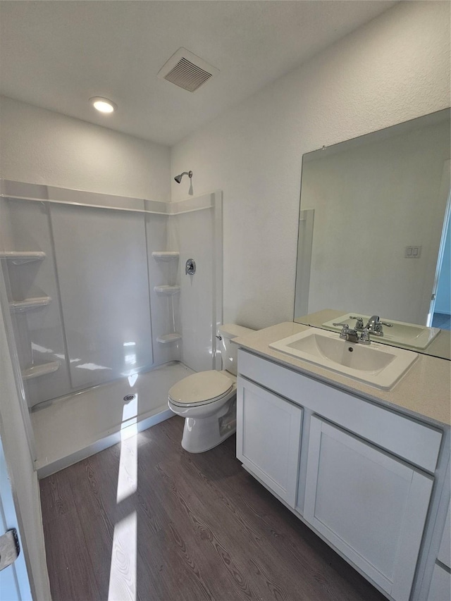 bathroom with visible vents, a shower, wood finished floors, vanity, and toilet
