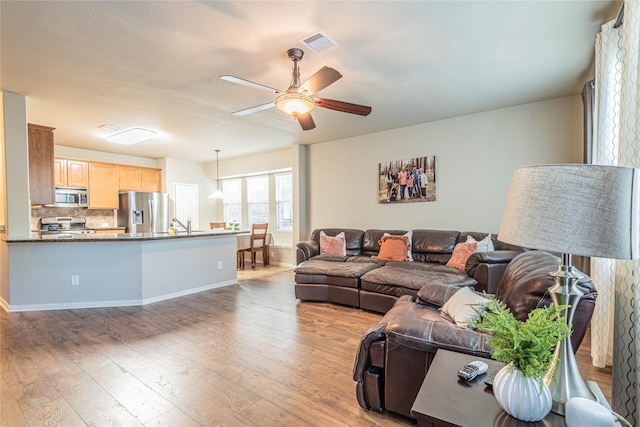 living area featuring baseboards, ceiling fan, light wood-type flooring, and visible vents