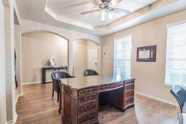 home office featuring a ceiling fan, baseboards, wood finished floors, and a raised ceiling