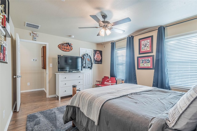 bedroom featuring visible vents, a ceiling fan, baseboards, and wood finished floors
