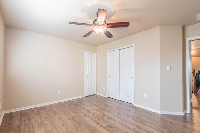 unfurnished bedroom featuring visible vents, a closet, wood finished floors, baseboards, and a ceiling fan