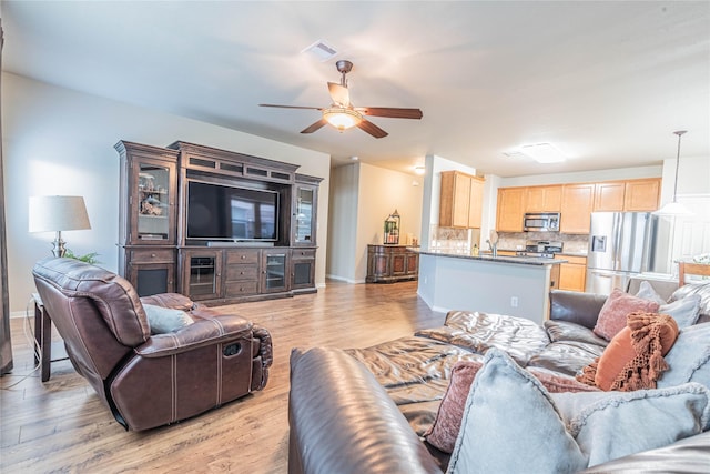 living area with visible vents, a ceiling fan, light wood-style flooring, and baseboards