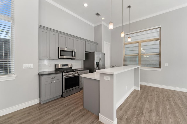 kitchen with appliances with stainless steel finishes, ornamental molding, gray cabinets, and light wood finished floors