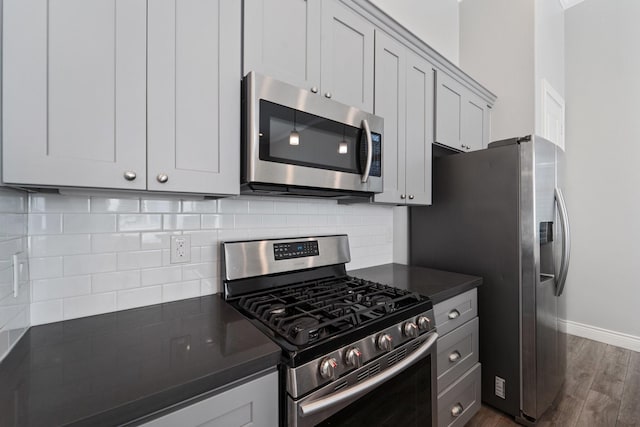 kitchen with dark countertops, appliances with stainless steel finishes, baseboards, decorative backsplash, and dark wood-type flooring