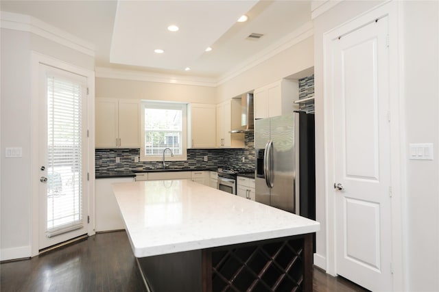 kitchen featuring crown molding, wall chimney range hood, a sink, stainless steel appliances, and tasteful backsplash