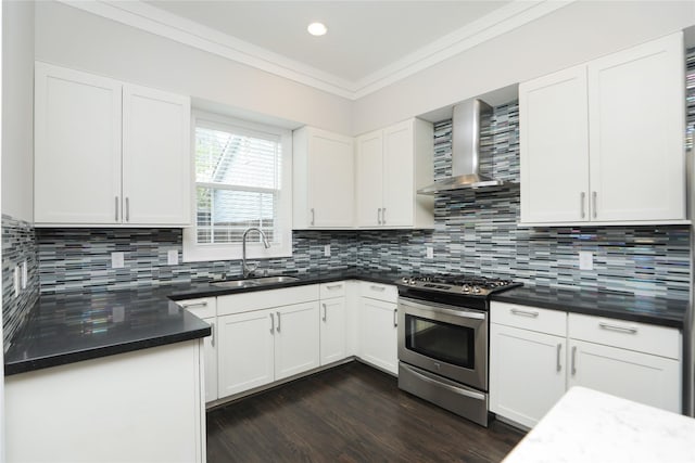 kitchen with stainless steel gas stove, dark countertops, wall chimney range hood, white cabinets, and a sink
