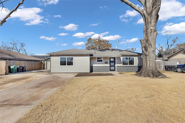 ranch-style house featuring fence, a shingled roof, brick siding, a front yard, and concrete driveway