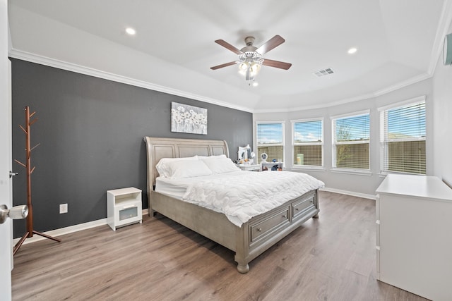 bedroom featuring crown molding, visible vents, light wood finished floors, and a raised ceiling
