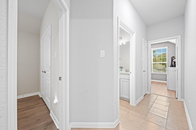 corridor featuring baseboards, a sink, and light tile patterned floors
