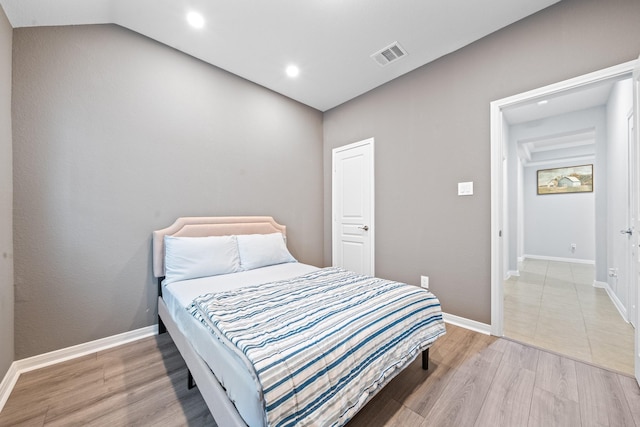 bedroom featuring baseboards, visible vents, lofted ceiling, and light wood-type flooring