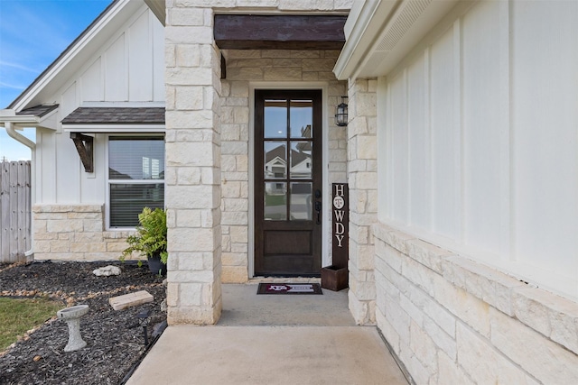 entrance to property featuring board and batten siding, fence, and stone siding