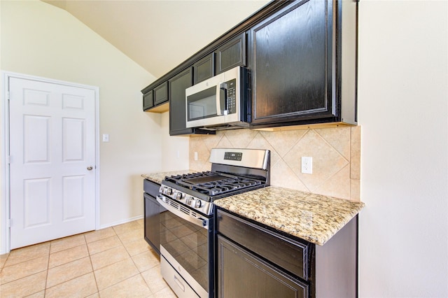 kitchen with appliances with stainless steel finishes, light stone counters, light tile patterned floors, lofted ceiling, and backsplash