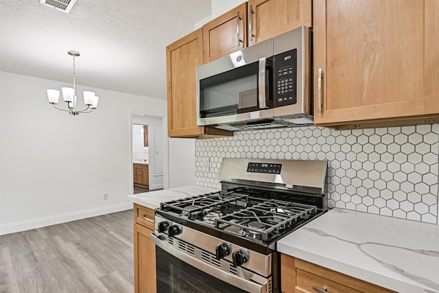 kitchen featuring a notable chandelier, light stone counters, stainless steel appliances, baseboards, and tasteful backsplash
