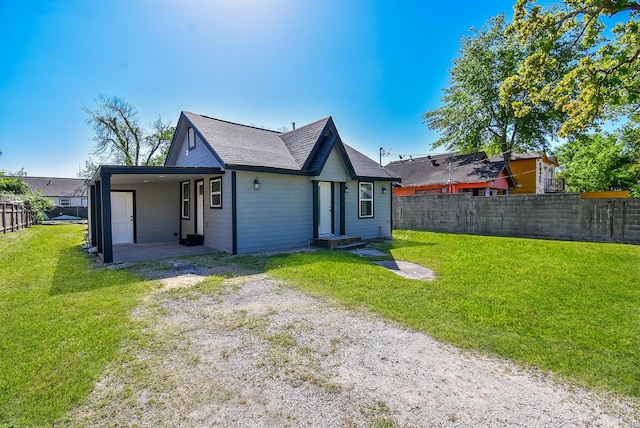 back of house featuring a lawn, fence, roof with shingles, and dirt driveway