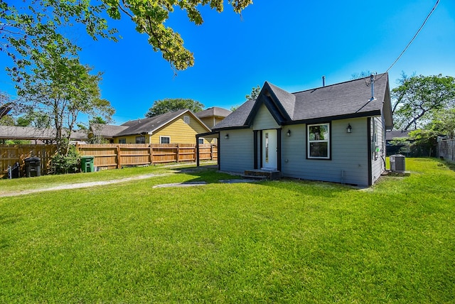 back of property featuring a yard, central AC unit, a fenced backyard, and roof with shingles