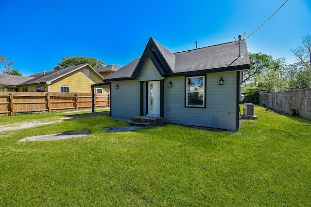 back of property featuring a fenced backyard, central AC unit, a yard, and roof with shingles