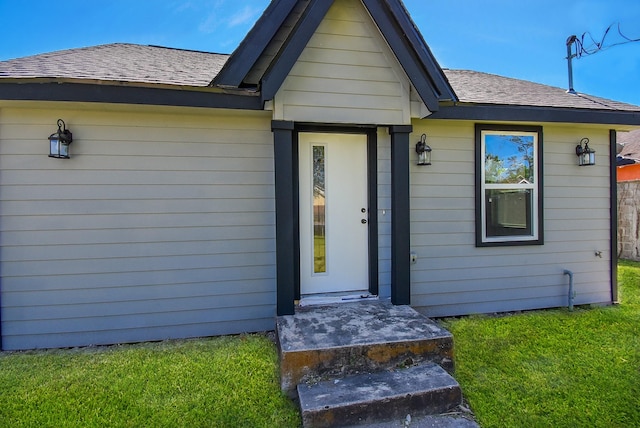 property entrance with a lawn and a shingled roof