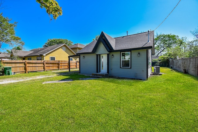 back of property with a fenced backyard, central AC unit, a yard, and roof with shingles