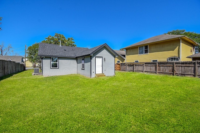 rear view of house with a lawn, central air condition unit, a shingled roof, and a fenced backyard