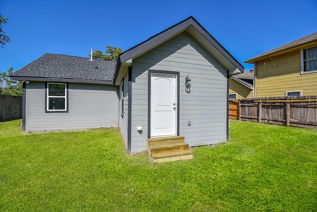 rear view of property featuring entry steps, a lawn, a fenced backyard, and roof with shingles